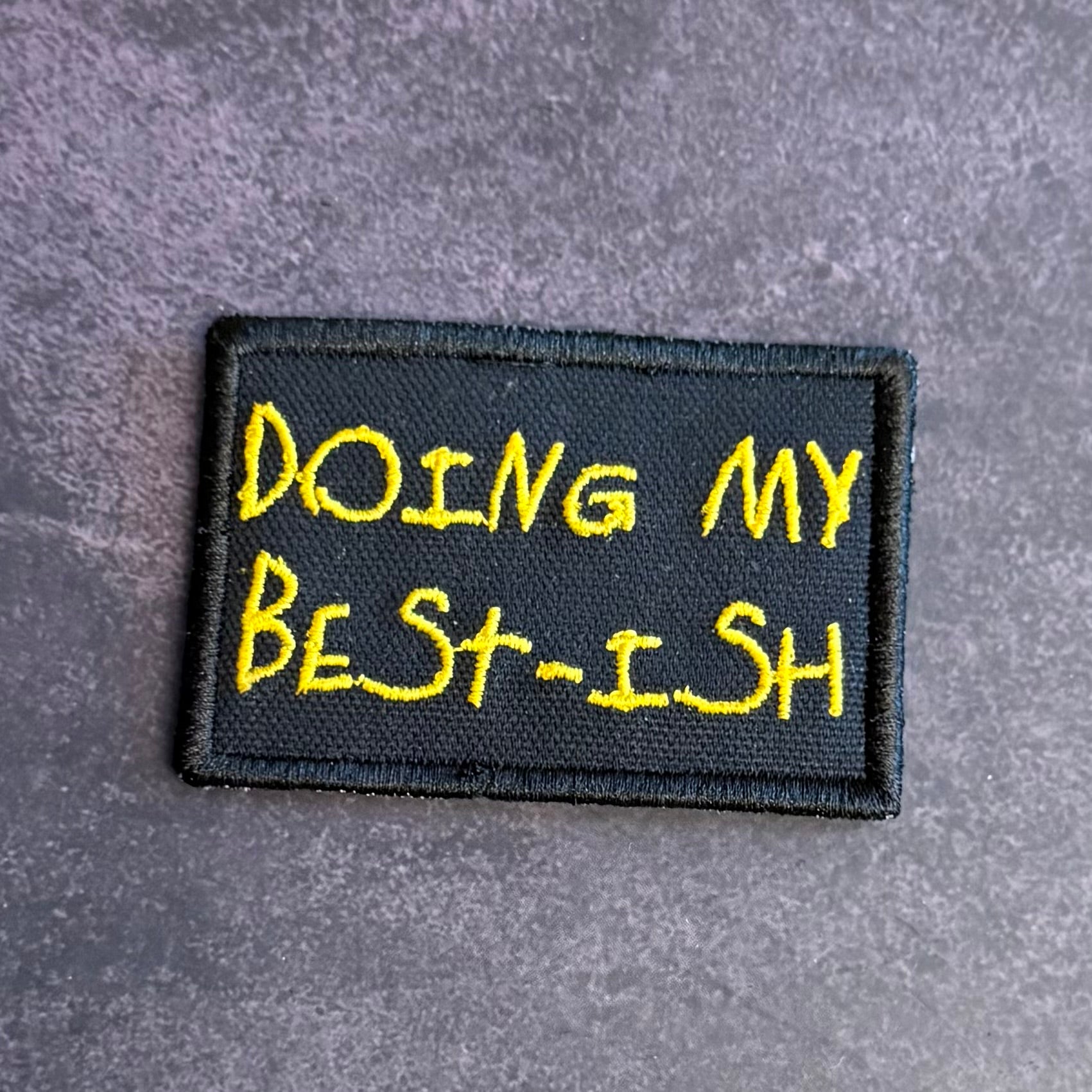A rectangular black embroidered patch with yellow text reading 'DOING MY BEST-ISH' on a textured gray background.