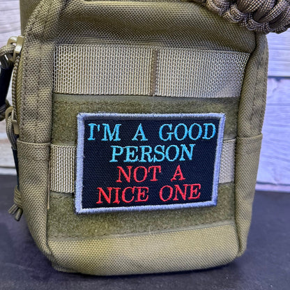A tactical utility pouch in olive drab nylon with a rectangular embroidered patch on the front. The patch has a black background with the text 'I'M A GOOD PERSON NOT A NICE ONE' in blue and red lettering, bordered in white.