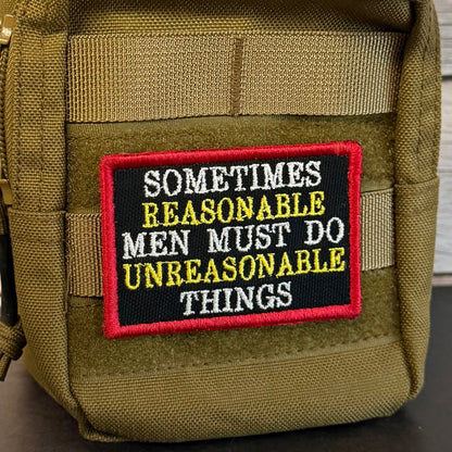 An olive green tactical pouch with a black embroidered patch featuring the text 'SOMETIMES REASONABLE MEN MUST DO UNREASONABLE THINGS' in white and yellow, with a red border.