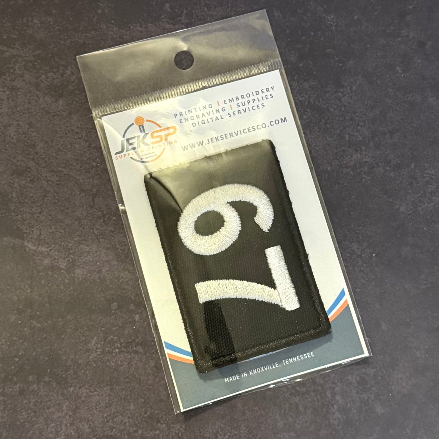 A black rectangular embroidered patch with a large white number 6, sealed in a clear plastic retail package with a printed backing card. The package shows the JEK Service Co branding and text including 'Printing & Embroidery' and 'Made in Knoxville, Tennessee'.