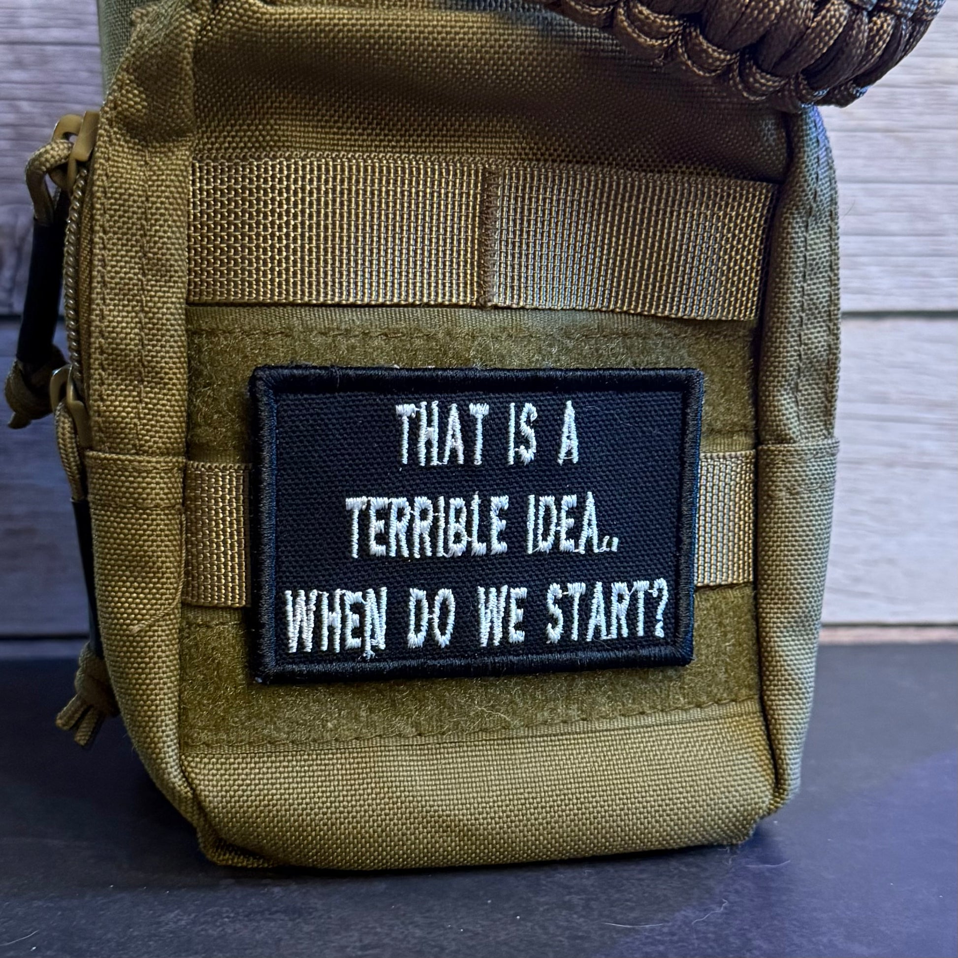 A close-up of a tactical pouch in olive drab nylon with a black rectangular patch featuring the white embroidered text 'THAT IS A TERRIBLE IDEA.