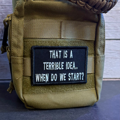 A close-up of a tactical pouch in olive drab nylon with a black rectangular patch featuring the white embroidered text 'THAT IS A TERRIBLE IDEA.