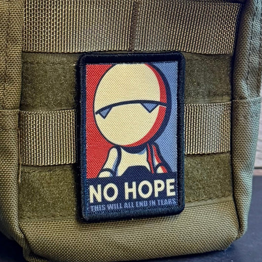 An olive green tactical pouch with a woven patch featuring a stylized figure and the text 'NO HOPE' and 'THIS WILL ALL END IN TEARS.' The pouch is shown close-up against a dark surface and wood background.