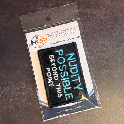 Nude Beach Warning embroidered morale patch: rectangular embroidered patch with light blue and white text reading 'NUDITY POSSIBLE BEYOND THIS POINT' in a clear plastic sleeve with a branded backing card from JEKSP Service Co.
