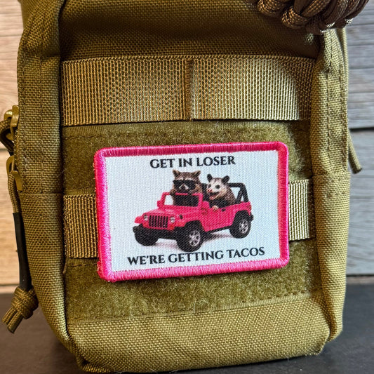 An olive green tactical pouch with a rectangular patch featuring a pink border and an illustration of two cartoon animals in a pink jeep with the text 'GET IN LOSER WE'RE GETTING TACOS'.