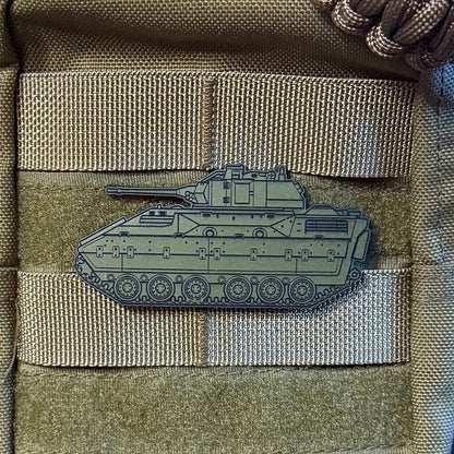 A close-up of a tactical pouch in olive drab canvas with MOLLE webbing, a paracord strap, and an embossed olive drab M2 Bradley tank patch on the front.