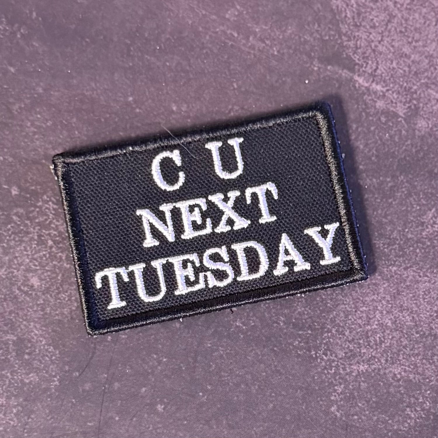A rectangular black embroidered patch with white text reading 'CU NEXT TUESDAY' on a textured dark gray background.