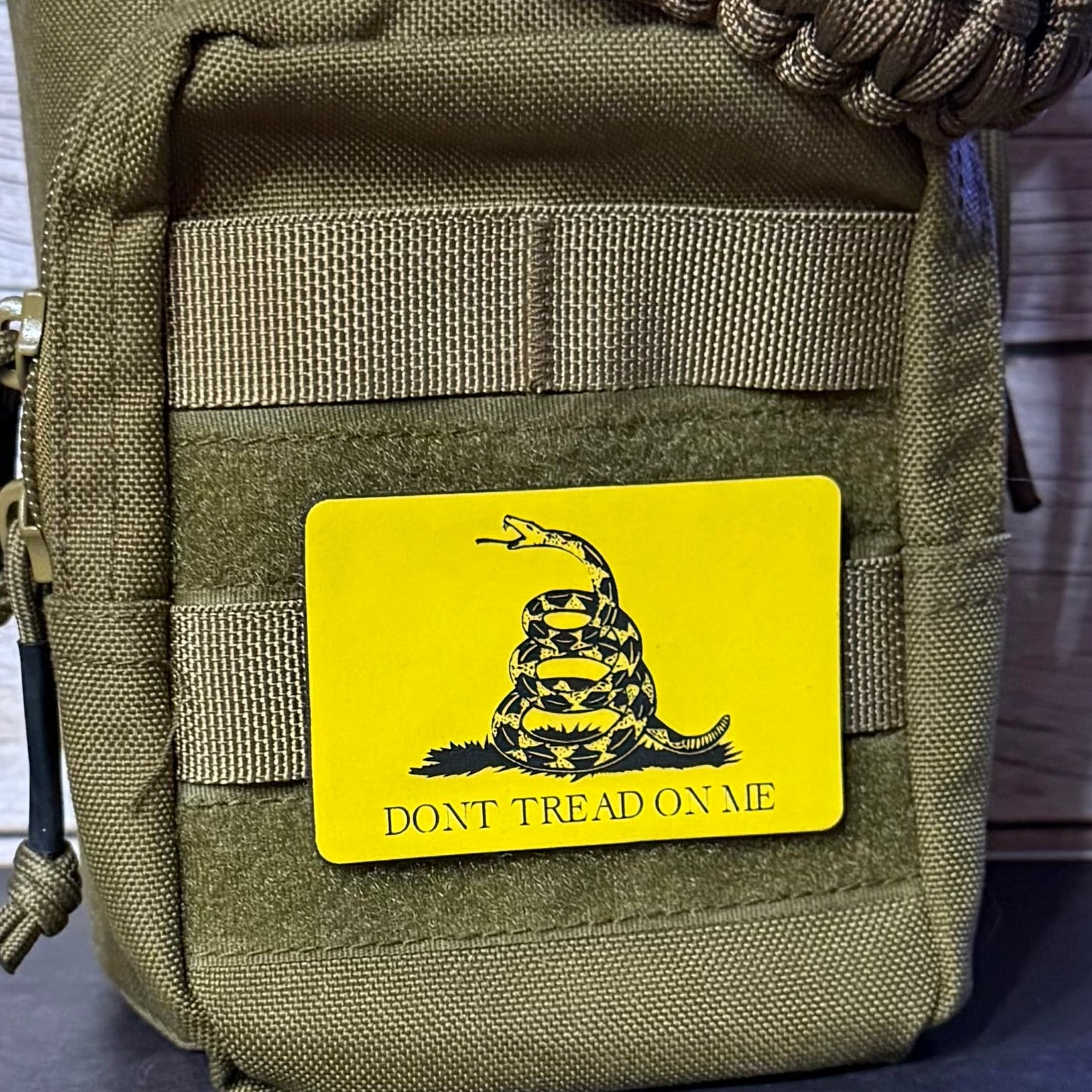 An olive drab tactical pouch with a bright yellow rectangular patch featuring the Gadsden flag design and the text 'DONT TREAD ON ME'.