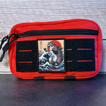 A red canvas utility pouch with black zippers and velcro strips, featuring a central patch with a Japanese-style cat illustration on a wave and red sun.