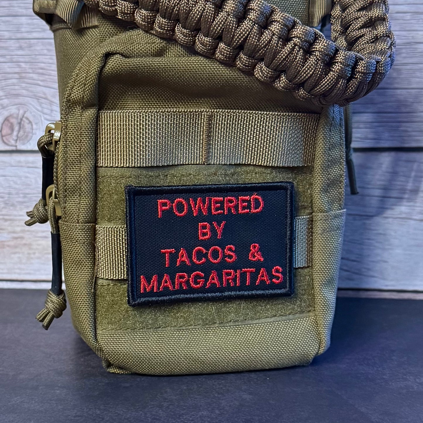 An olive green tactical pouch with a woven strap, featuring a black patch with red embroidered text that reads 'POWERED BY TACOS & MARGARITAS'.