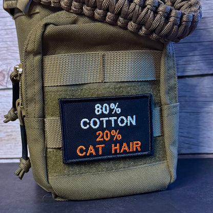 An olive green tactical pouch with a woven brown paracord strap, featuring a black embroidered patch that reads '80% COTTON 20% CAT HAIR'.
