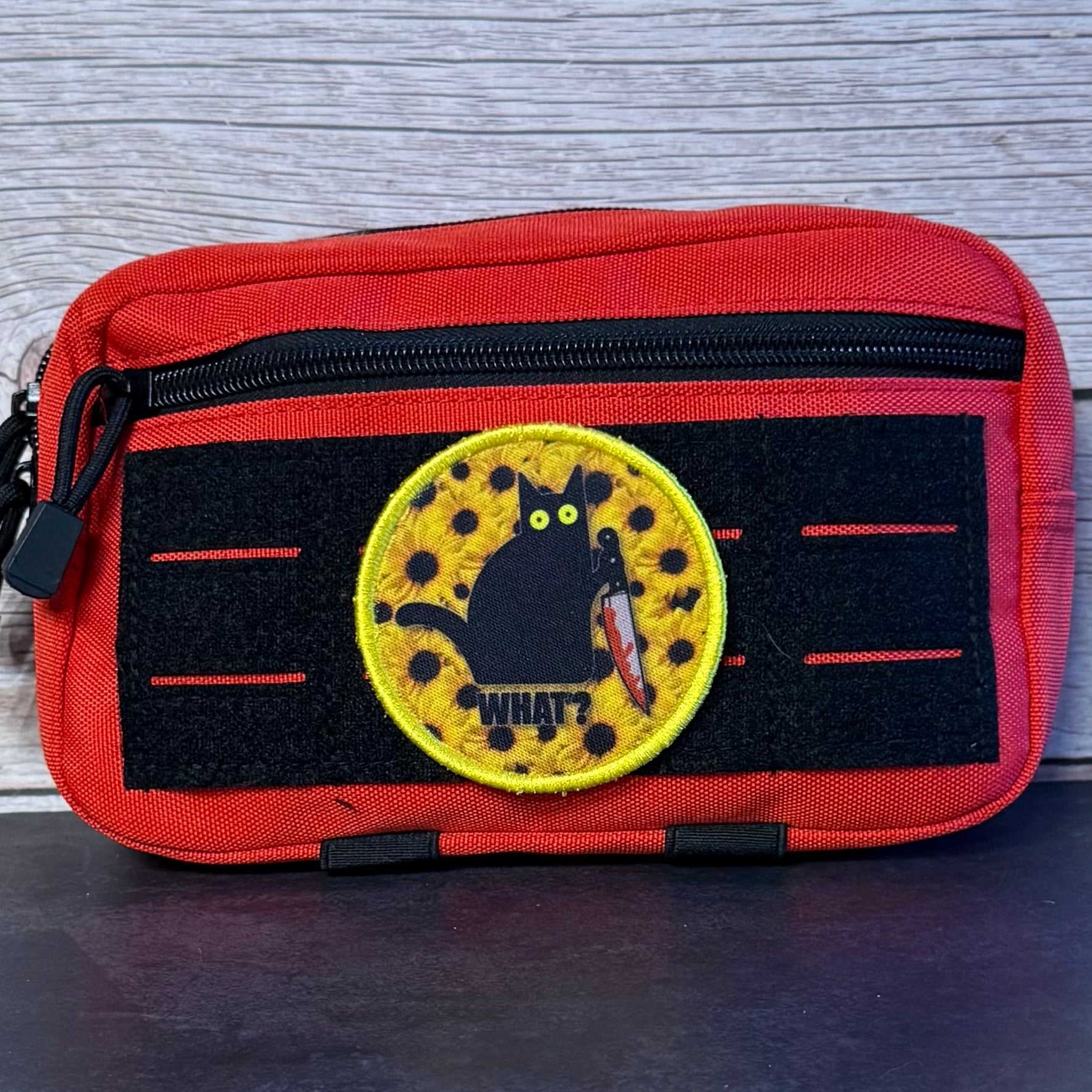 A red and black tactical pouch featuring a circular embroidered patch with a black cat holding a knife and the text 'WHAT?'.