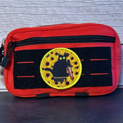 A red and black tactical pouch featuring a circular embroidered patch with a black cat holding a knife and the text 'WHAT?'.