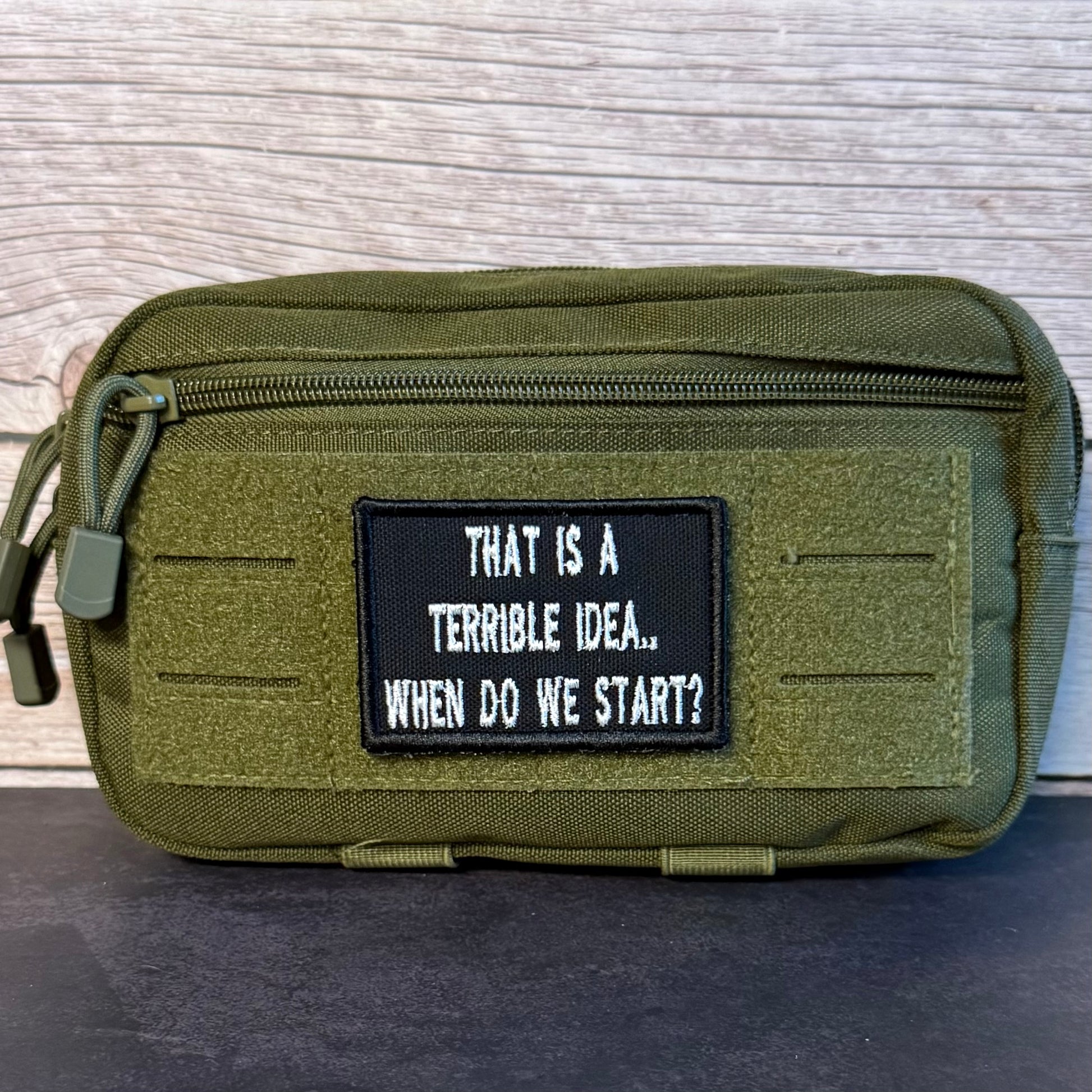 An olive green tactical pouch with a black rectangular patch that reads 'THAT IS A TERRIBLE IDEA.