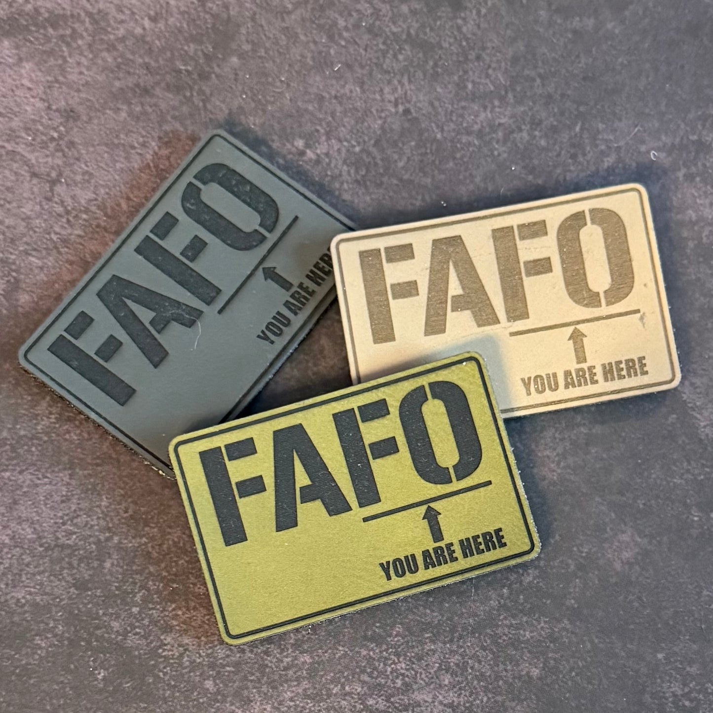 Three rectangular tactical patches with the text 'FAFO' and 'YOU ARE HERE' arranged on a textured gray background.