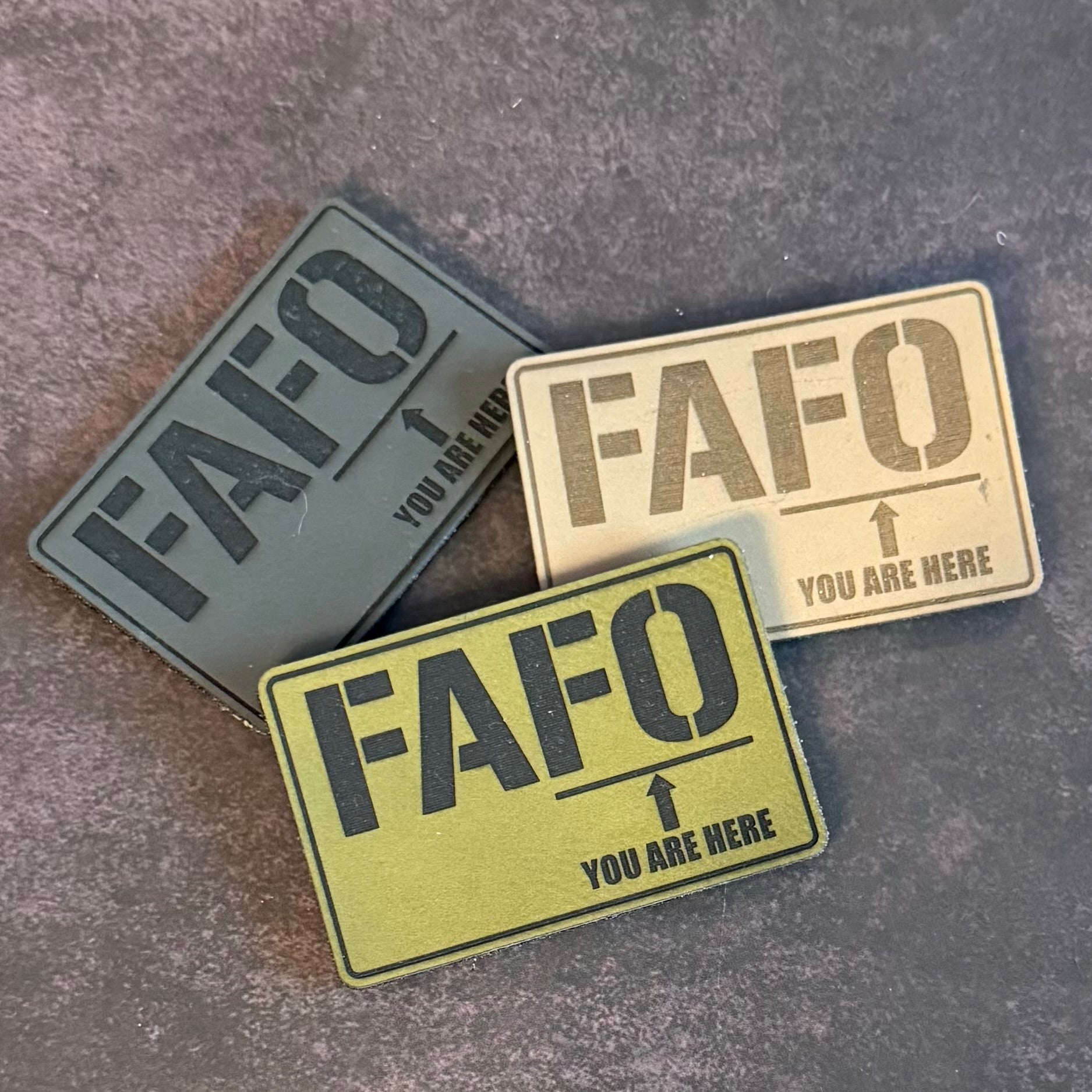Three rectangular tactical patches with the text 'FAFO' and 'YOU ARE HERE' arranged on a textured gray background.
