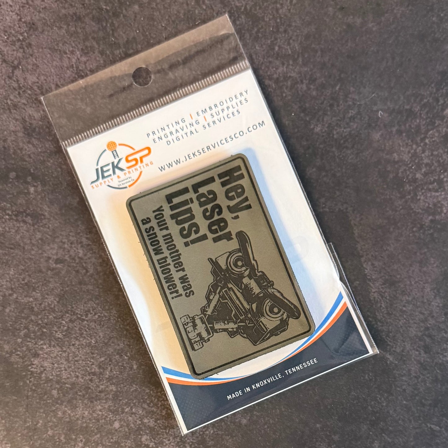A rectangular embroidered patch in clear retail packaging, featuring a motorcycle illustration and the text 'Hey, Laser! LIPS! HOW RIDE WAS BAD' on a dark gray textured background.