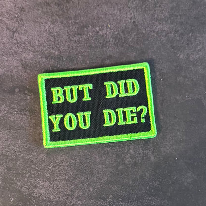 A rectangular embroidered patch with a black background and bright neon green border and text reading 'BUT DID YOU DIE?' on a dark textured surface.