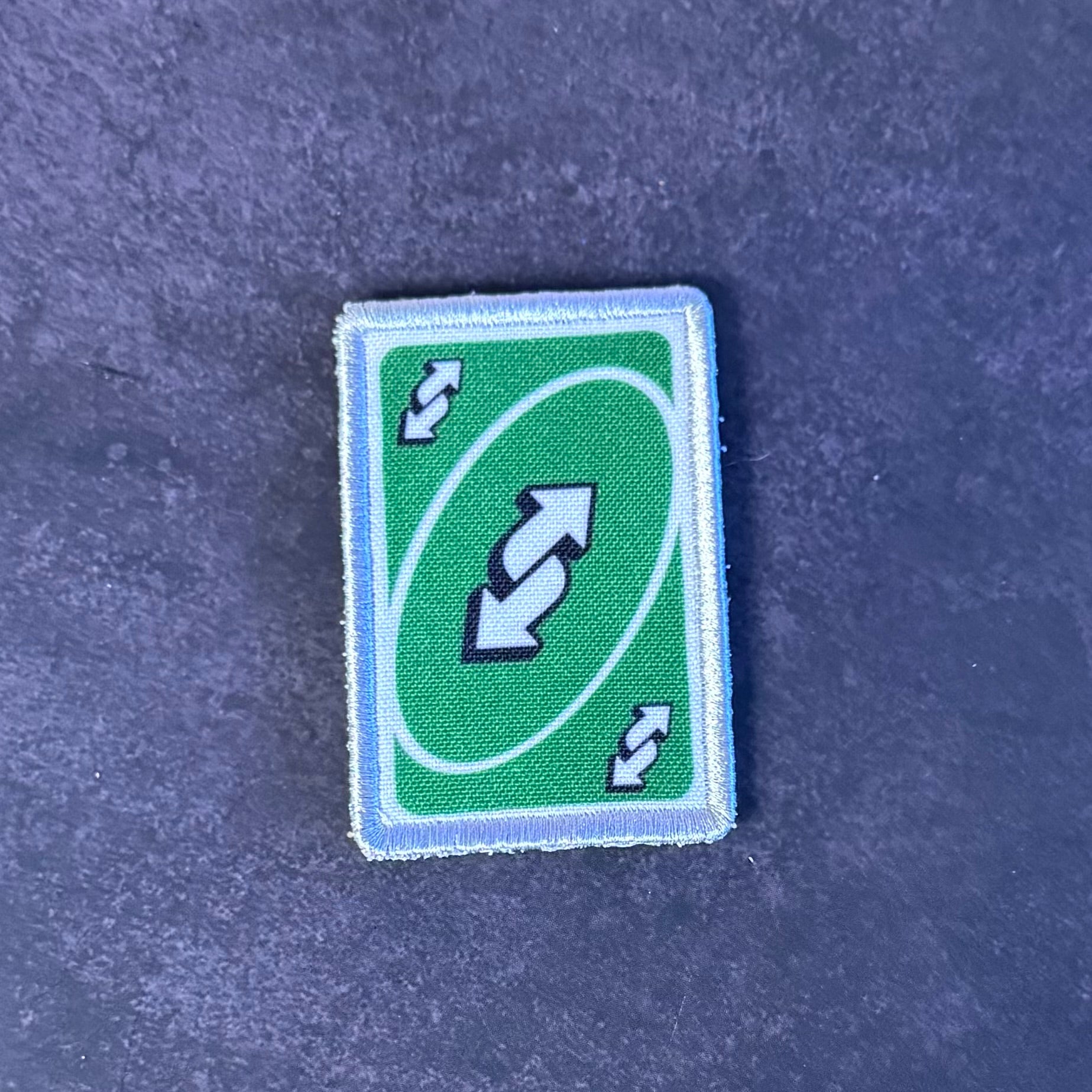 A rectangular green patch with a white border and a double-arrow symbol, placed on a textured dark blue surface.