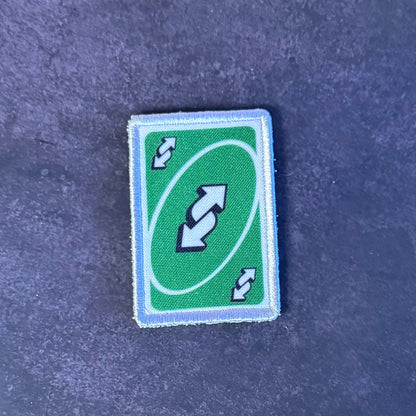 A rectangular green patch with a white border and a double-arrow symbol, placed on a textured dark blue surface.