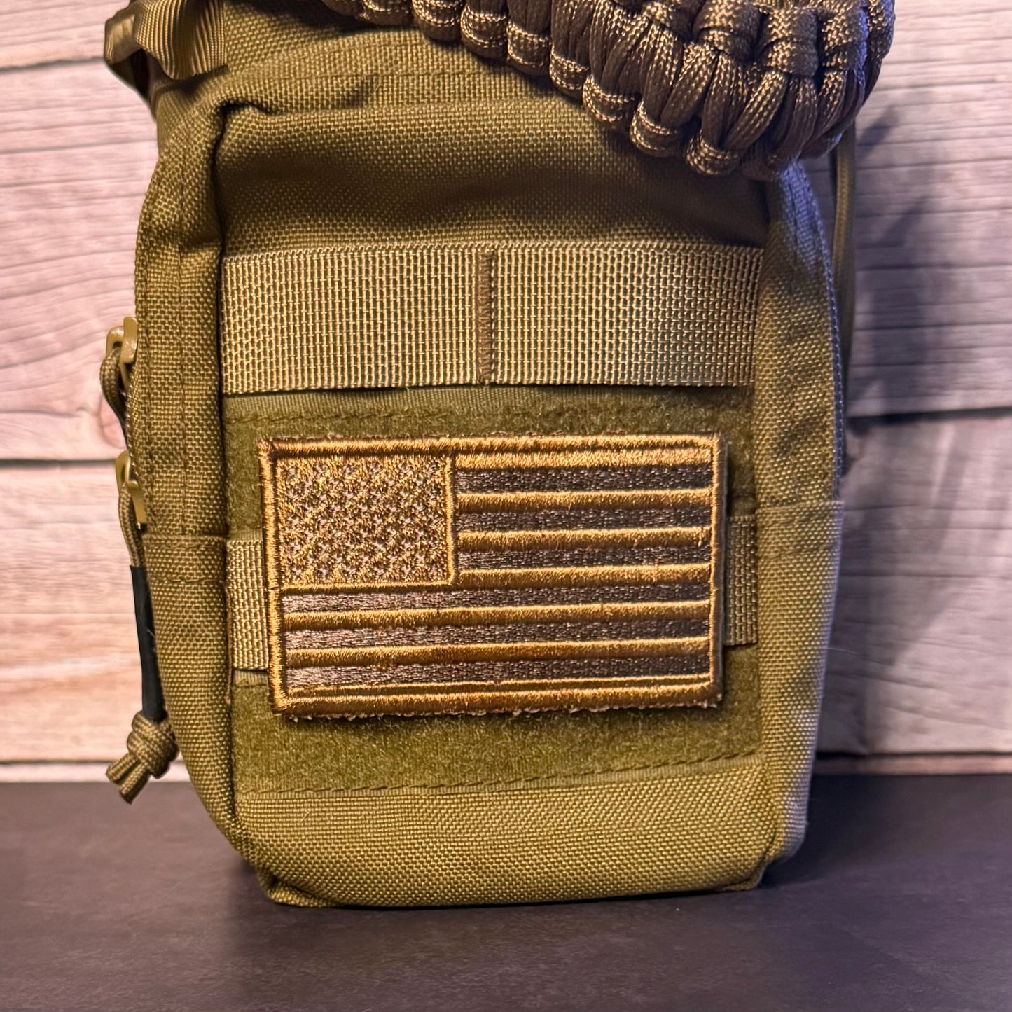 An coyote brown tactical pouch with a US flag patch on the front, featuring a paracord strap at the top, set against a rustic wood background.