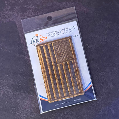 A tactical embroidered American flag patch in its original retail packaging, displayed on a dark textured surface. The packaging features the JEKSP Embroidery Supplies logo.
