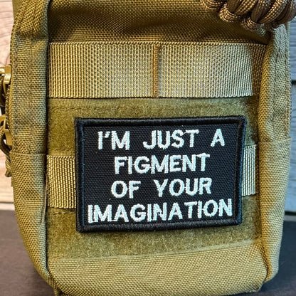 Close-up of a tactical pouch in olive drab green with a black embroidered patch that reads 'I'M JUST A FIGMENT OF YOUR IMAGINATION' in white text.