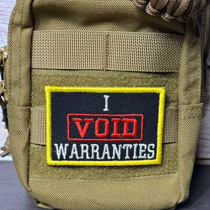 A close-up of a tactical pouch in olive drab nylon with a rectangular embroidered patch that reads 'I VOID WARRANTIES' in red, white, and black with a yellow border.