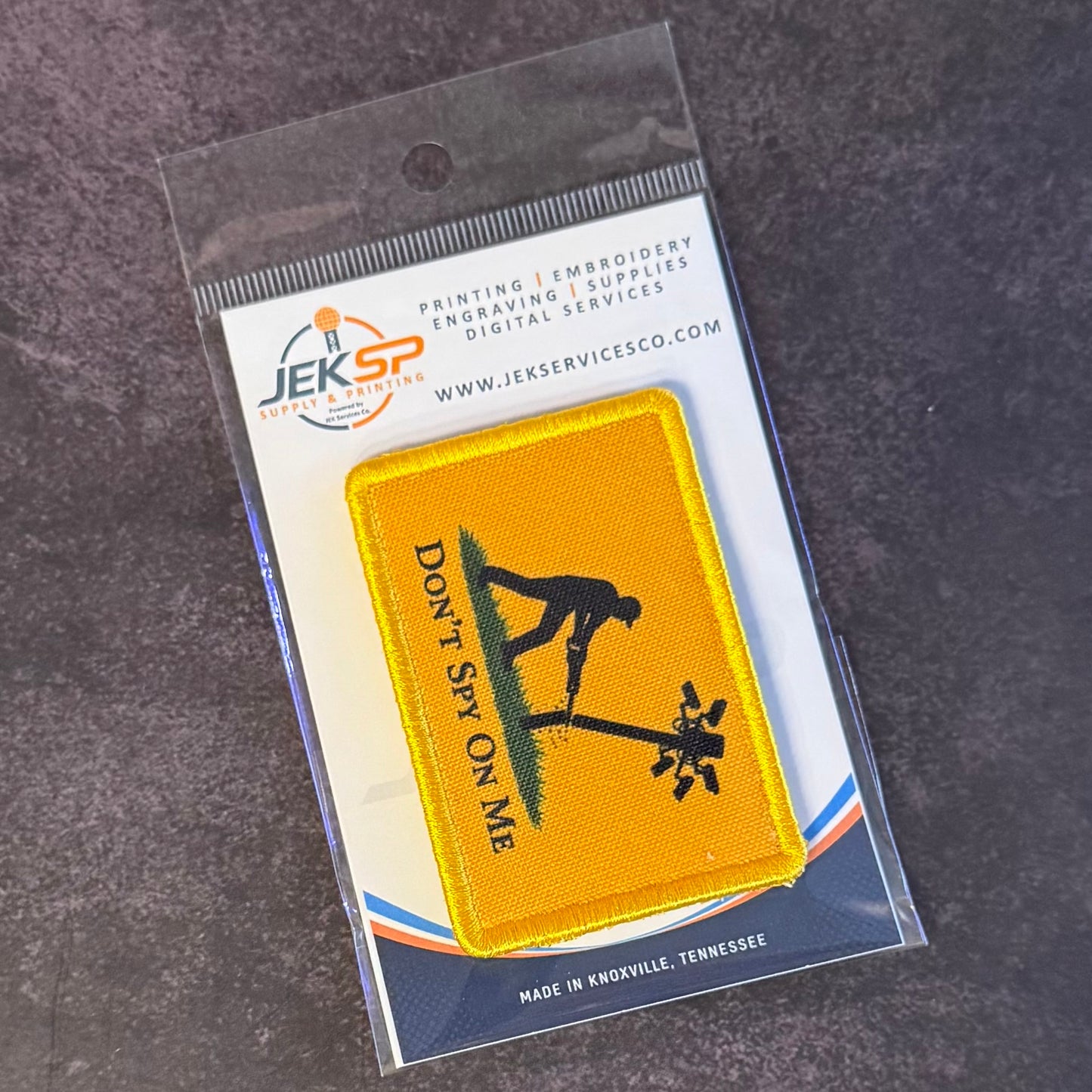 A yellow embroidered patch with a black silhouette of a person sitting on a seesaw and the text 'DON'T SAY ON ME' in black, packaged on a branded JEKSP Special Order card over a dark gray textured surface.