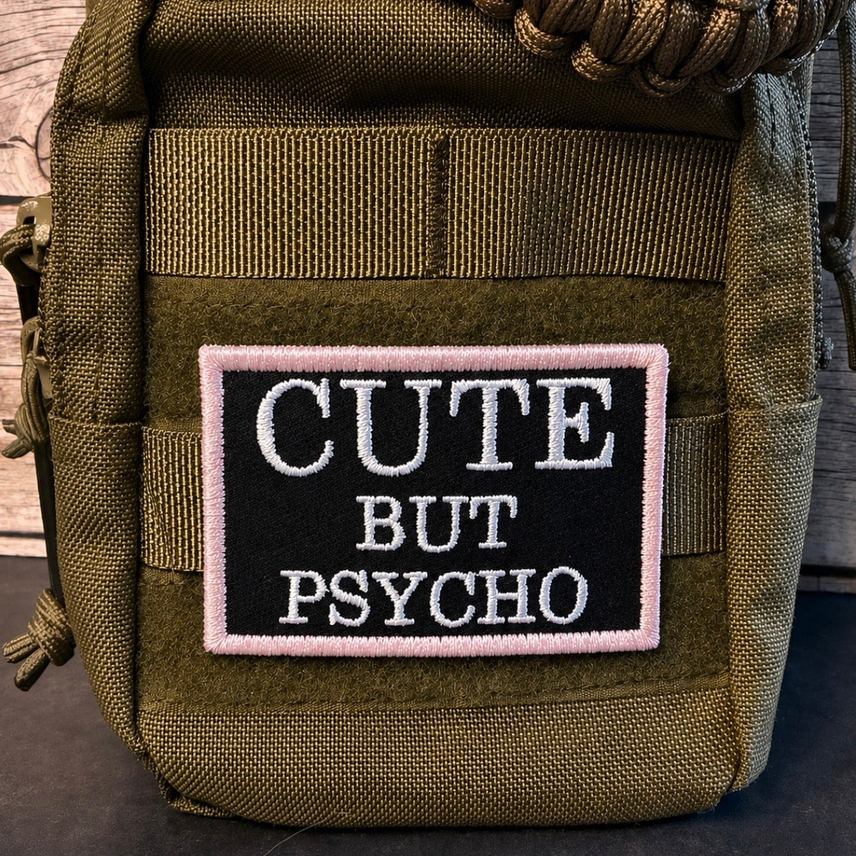 An olive green tactical pouch featuring a rectangular embroidered patch with the text 'CUTE BUT PSYCHO' in white on a black background with a pink border.