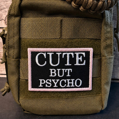 An olive green tactical pouch featuring a rectangular embroidered patch with the text 'CUTE BUT PSYCHO' in white on a black background with a pink border.