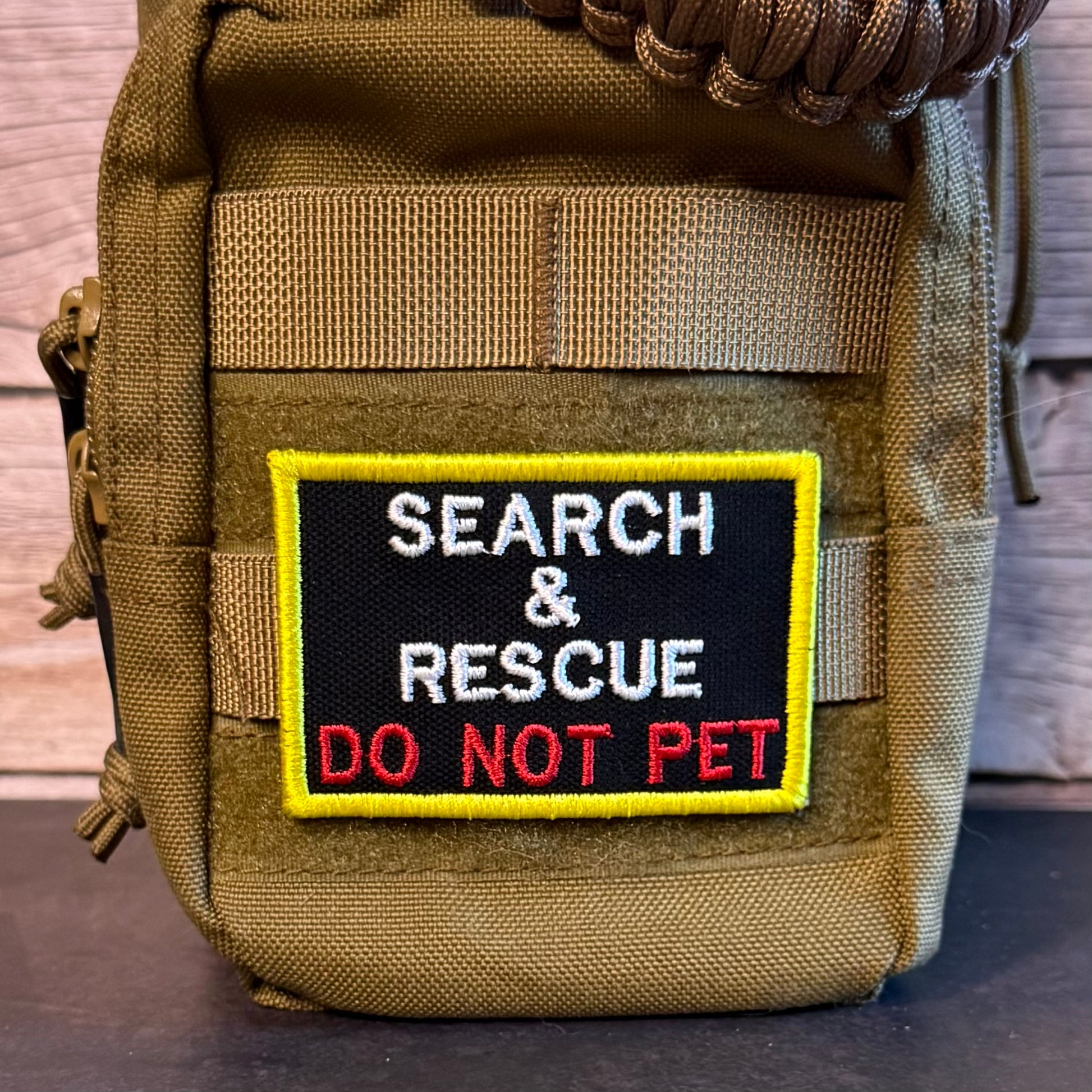 A tactical pouch in olive drab nylon with a rectangular embroidered patch that reads 'SEARCH & RESCUE DO NOT PET' in white and red on a black background with a yellow border.