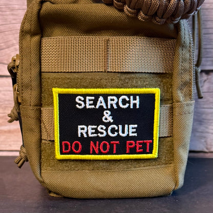 A tactical pouch in olive drab nylon with a rectangular embroidered patch that reads 'SEARCH & RESCUE DO NOT PET' in white and red on a black background with a yellow border.