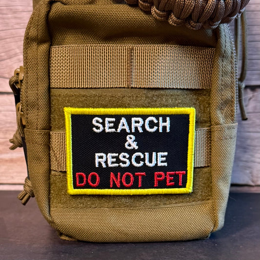 A tactical pouch in olive drab nylon with a rectangular embroidered patch that reads 'SEARCH & RESCUE DO NOT PET' in white and red on a black background with a yellow border.