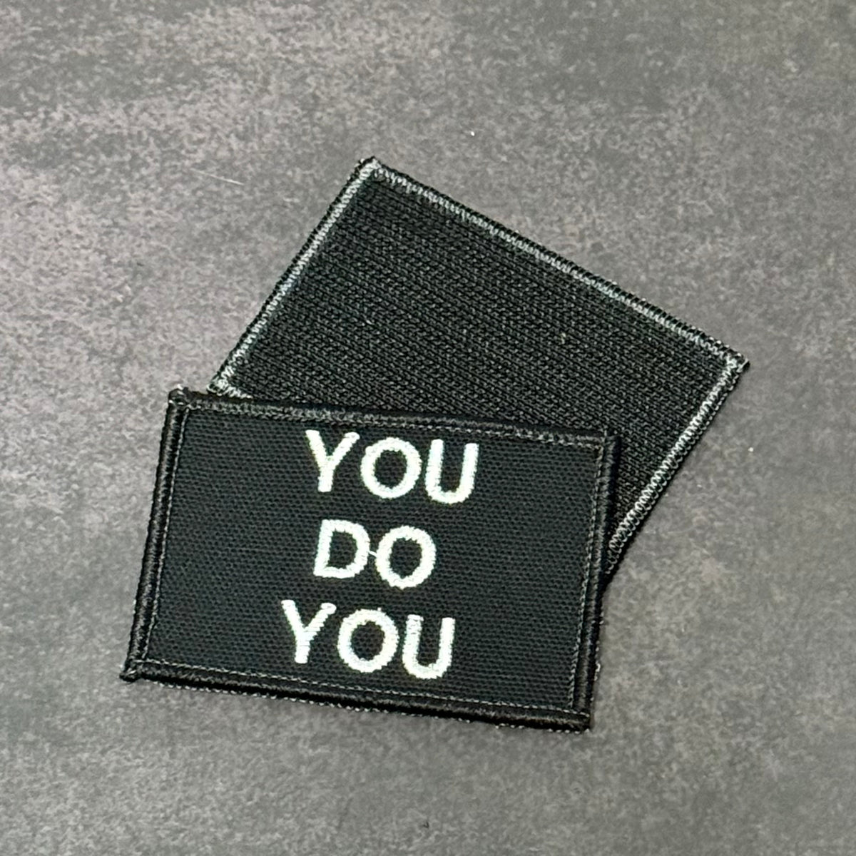 Two rectangular black embroidered patches with white text reading 'YOU DO YOU' on a textured gray background.
