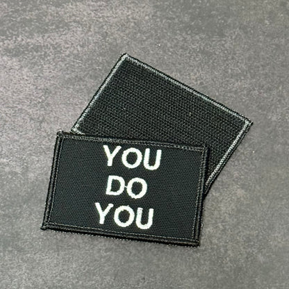 Two rectangular black embroidered patches with white text reading 'YOU DO YOU' on a textured gray background.