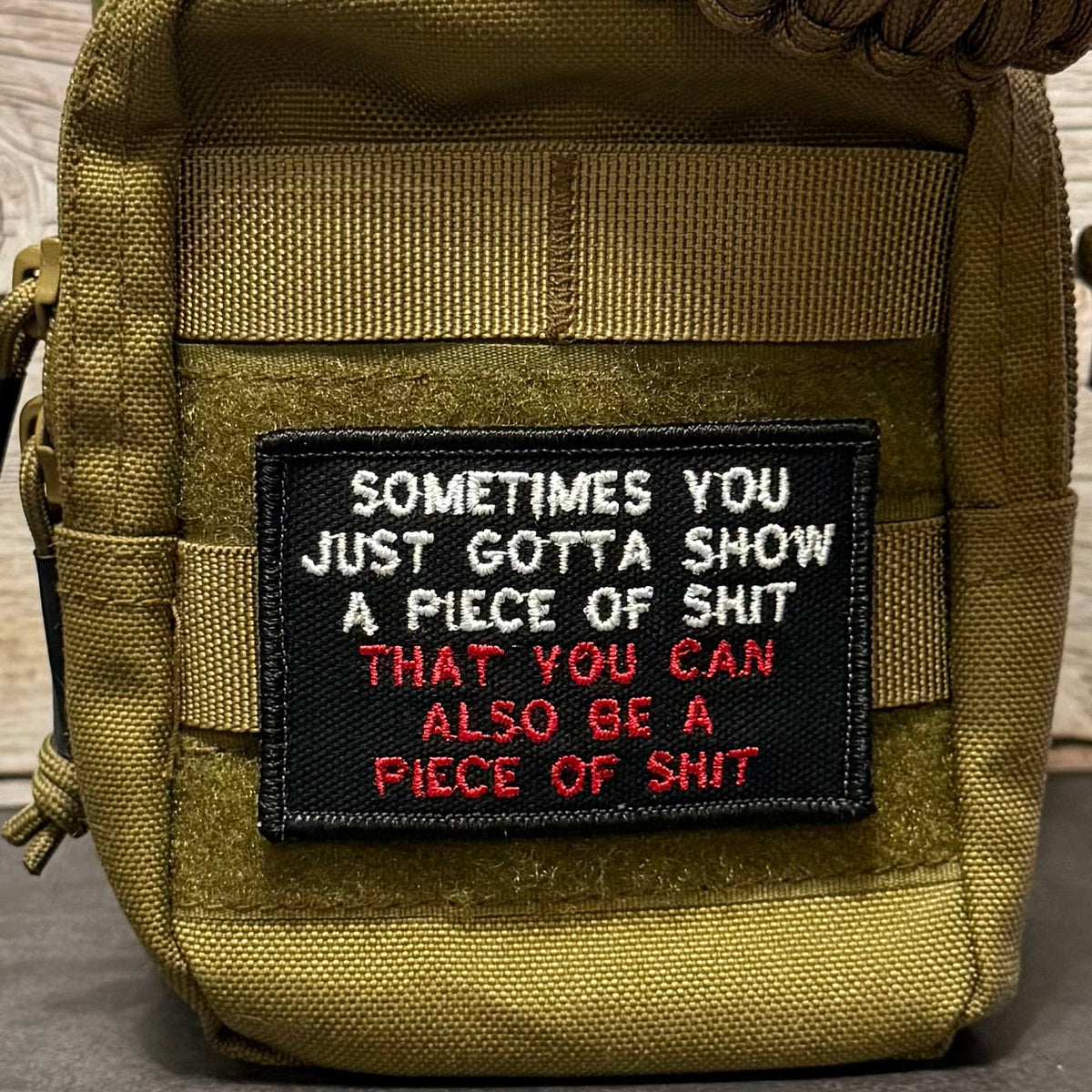 An olive drab tactical pouch with a black embroidered patch featuring the text 'SOMETIMES YOU JUST GOTTA SHOW A PIECE OF SHIT THAT YOU CAN ALSO BE A PIECE OF SHIT' in white and red lettering.