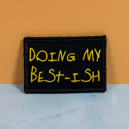A rectangular black embroidered patch with yellow text reading 'DOING MY BEST-ISH' against a two-tone orange and light gray background.