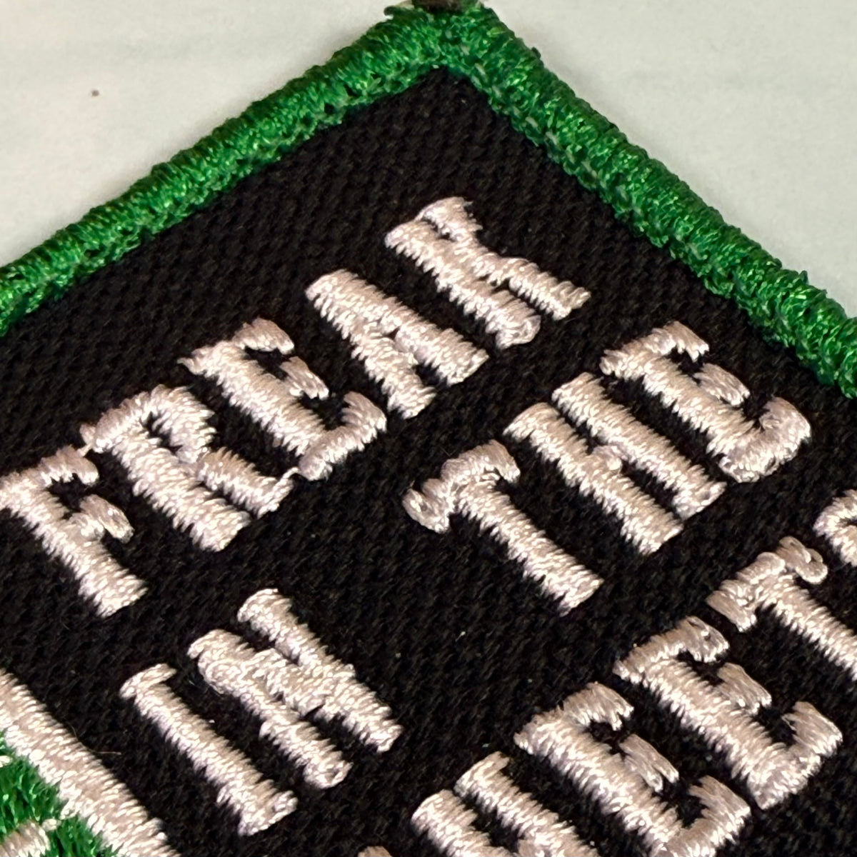 Close-up of an embroidered patch with a black background, green border, and white text reading 'FREEDOM IN THE HEART'.