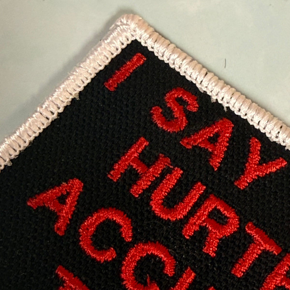 Close-up of a black embroidered patch with red text reading 'I SAY HURTE ACC.