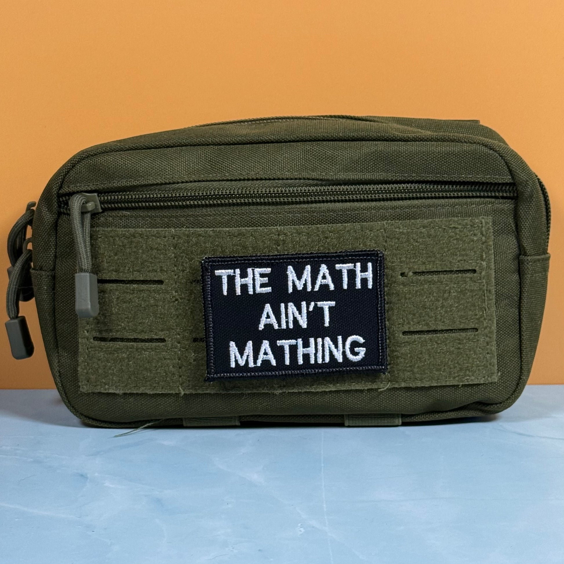 An olive green tactical pouch with a black patch that reads 'THE MATH AIN'T MATHING' in white text, set against a split orange and light blue background.