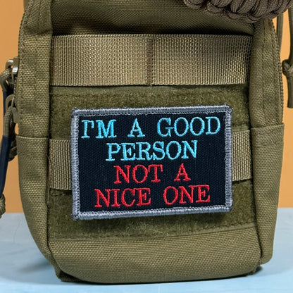An olive green tactical pouch with a rectangular embroidered patch that reads 'I'M A GOOD PERSON NOT A NICE ONE' in blue and red text on a black background.