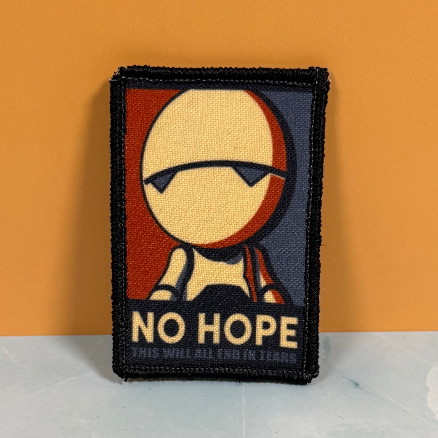 A rectangular embroidered patch with a black border, featuring a stylized face with sunglasses and the text 'NO HOPE' and 'THIS WILL ALL END IN TEARS' against a warm orange and dark blue background.
