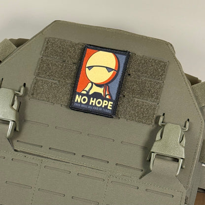 A rectangular tactical patch featuring a stylized face with sunglasses and the text 'NO HOPE' in yellow, attached to olive drab MOLLE webbing on a tactical plate carrier vest.