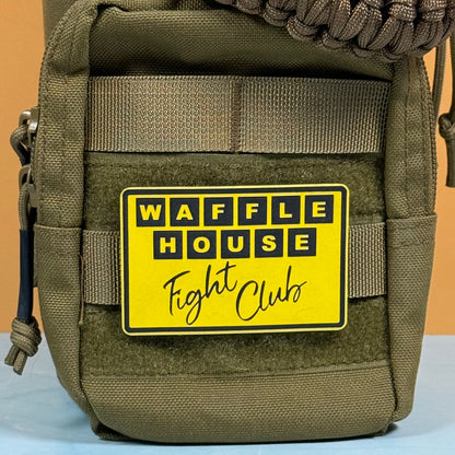 An olive green tactical pouch with a yellow and black 'WAFFLE HOUSE Fight Club' patch, shown against a solid orange background.