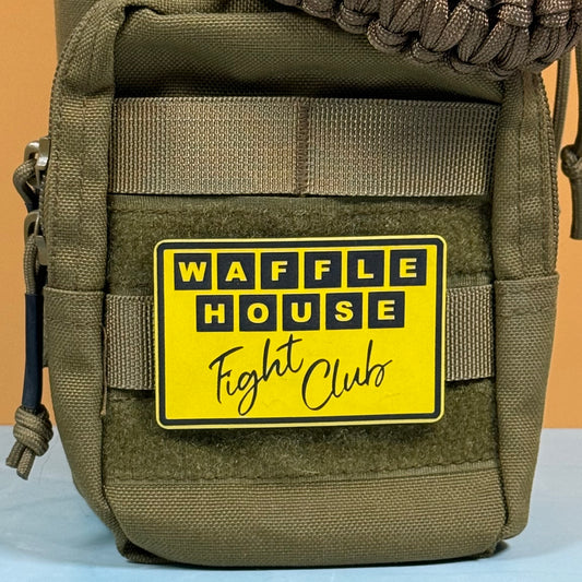 An olive green tactical pouch with a yellow and black 'WAFFLE HOUSE Fight Club' patch, shown against a solid orange background.