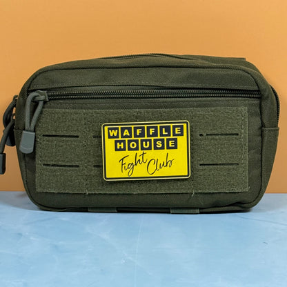 An olive green tactical pouch with a yellow 'WAFFLE HOUSE Fight Clubs' patch on the front, set against a solid orange background and light blue surface.