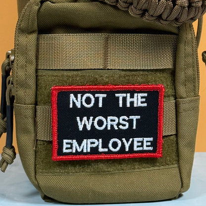 An olive green tactical pouch featuring a rectangular embroidered patch with the text 'NOT THE WORST EMPLOYEE' in white on a black background, bordered in red.