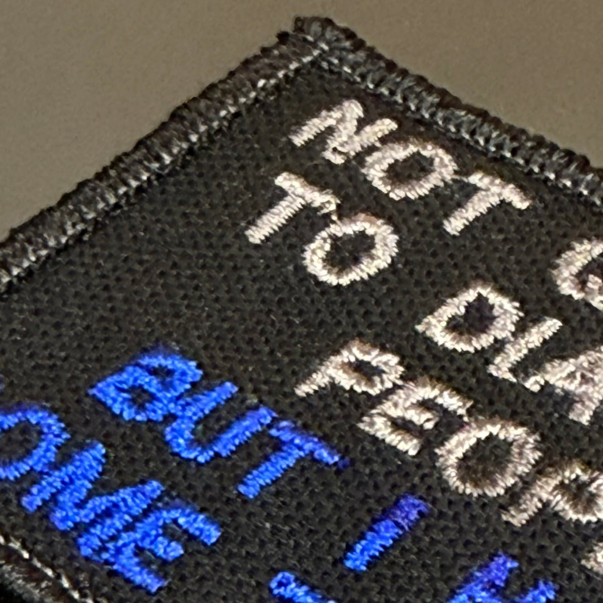 Close-up of a black embroidered patch with white and blue text reading 'NOT GUILTY TO PEOPLE BUT I H.