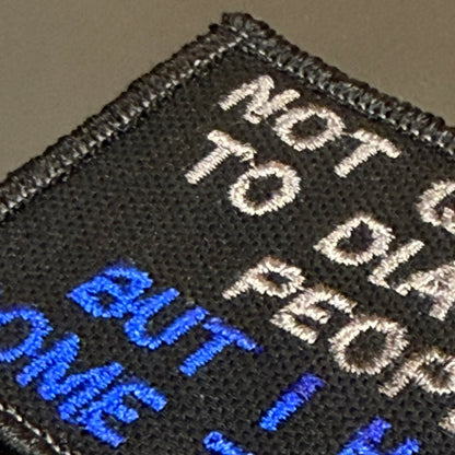 Close-up of a black embroidered patch with white and blue text reading 'NOT GUILTY TO PEOPLE BUT I H.